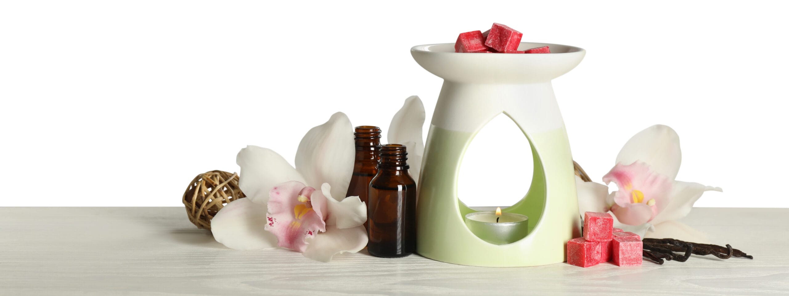 Composition of an aroma lamp featuring wax melts, framed by essential oil bottles on a light grey table against white background